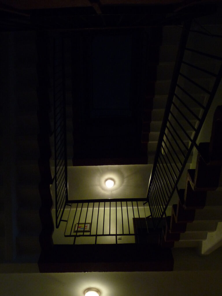 Laluan tangga yang gelap di dalam sebuah apartment, memberikan suasana seram.